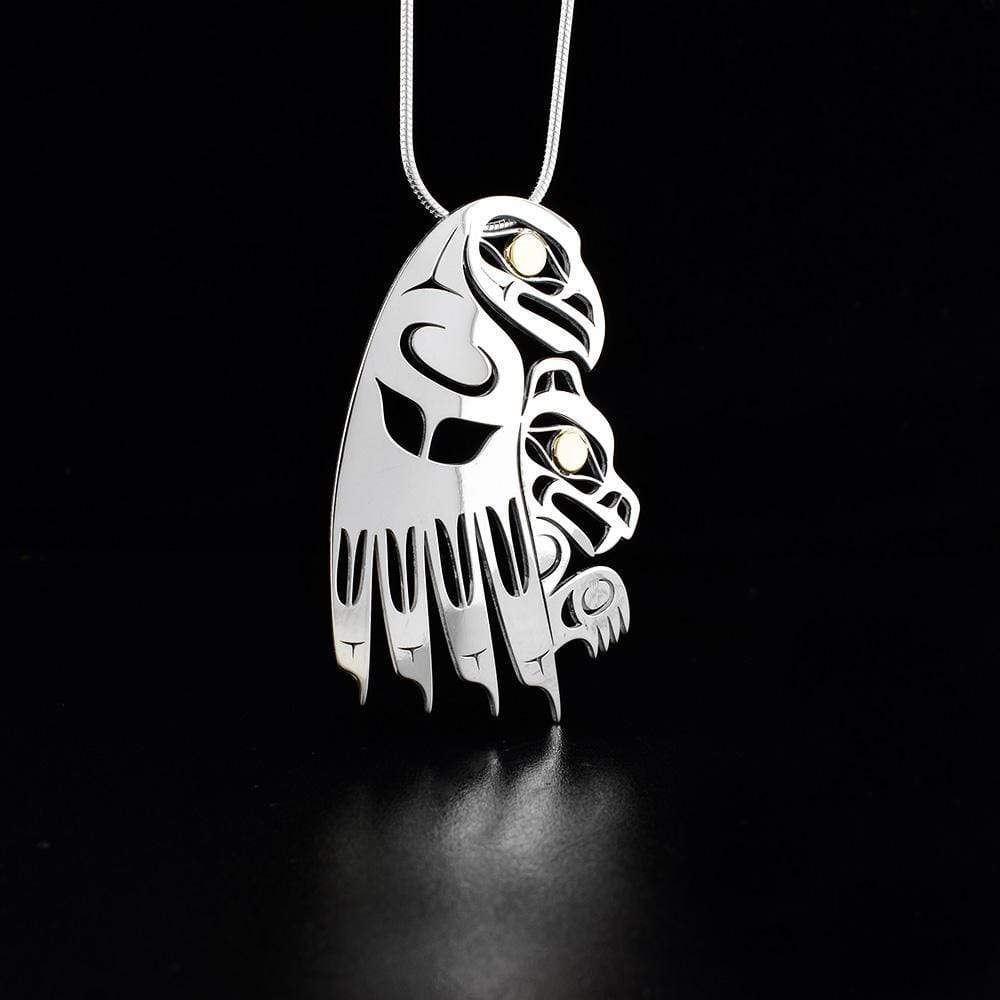 This Bear and Eagle pendant is made from sterling silver and 18K gold. The piece is shaped like and has cutout designs that depict the Eagle carrying the Bear and their eyes are made from gold.