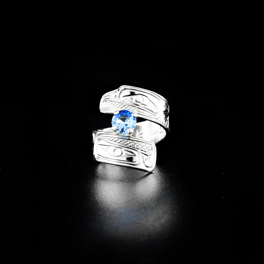 Eagle and raven wrap ring hand-carved by Coast Salish and Cree artist Richard Lang. Made of sterling silver and a lab-grown stone. Band is 0.31" wide, with the flexible wrap design giving the ring a comfortable fit. Size 7.