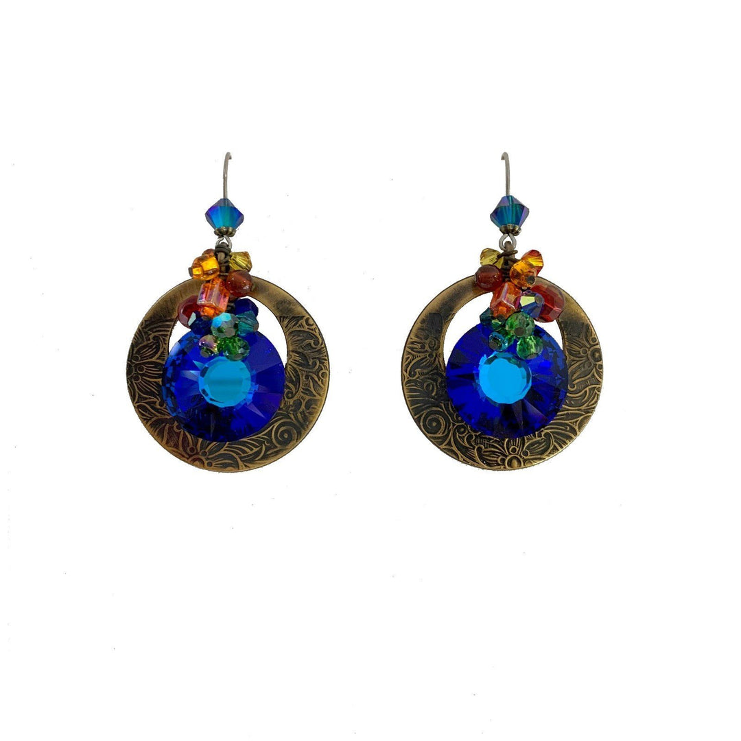 These Swarovski crystal dangle earrings are made from glass, Swarovski crystals and hand worked brass to create this piece. There is a large, circle cutout hangs made from brass with large, dark blue crystals hanging beside them. There are clusters of glass beads and crystals featured on the piece.