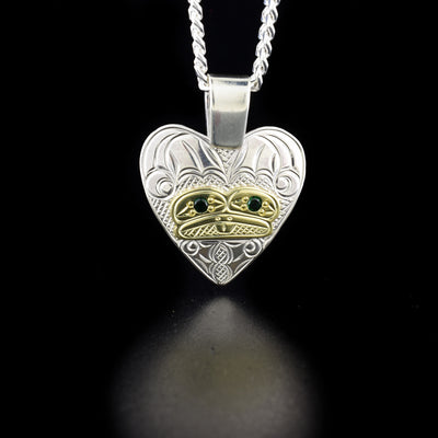 Gold and Silver Frog Heart Pendant with Green Stones hand-carved by Coast Salish and Cree artist Richard Lang. He has used sterling silver and 14K gold to create this piece and set a dark green lab-created stone in both eyes of the frog. Pendant measures 1.50" x 1.19" including bail. Chain not included.