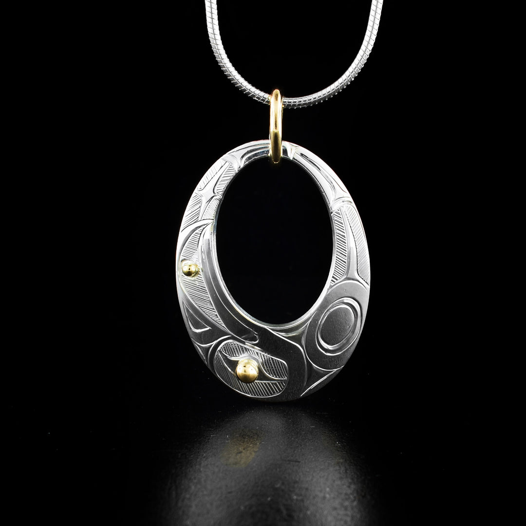 Gold and Silver Oval Cut Out Raven Pendant hand-carved by Haisla artist Hollie Bartlett. There is 14K gold in the eye and beak of the raven and the rest of the piece is sterling silver. Bail is gold-filled. Pendant measures 1.40" x 0.80" including bail. Chain not included.