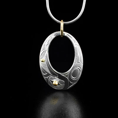 Gold and Silver Oval Cut Out Raven Pendant hand-carved by Haisla artist Hollie Bartlett. There is 14K gold in the eye and beak of the raven and the rest of the piece is sterling silver. Bail is gold-filled. Pendant measures 1.40" x 0.80" including bail. Chain not included.