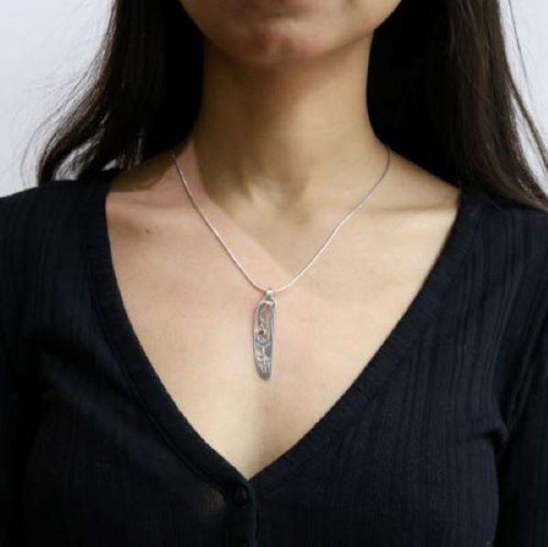 This Raven feather pendant is made from sterling silver and 18K gold. The pendant is feather shaped and has cutout designs that depict the Raven and its eyes are made from gold.