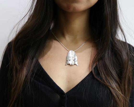 This large silver pendant is made from sterling silver and 18K gold. The piece is shaped like and has cutouts that depict three watchmen with golden eyes. The watchmen are positioned facing outward in a circle.