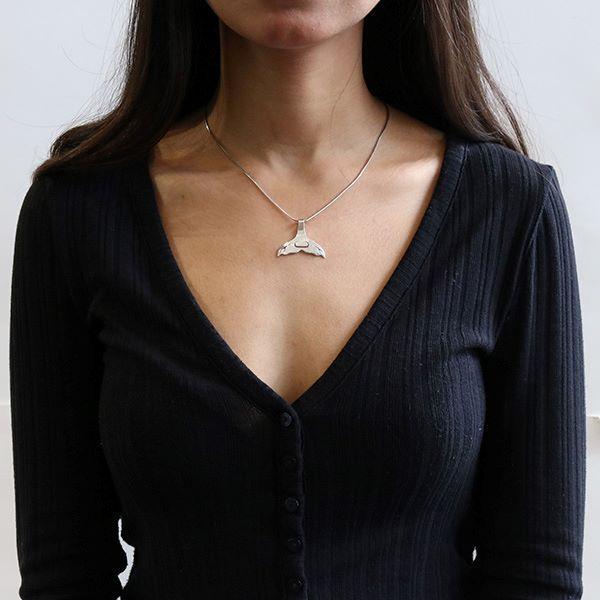 This whale tail pendant is made from sterling silver and is shaped like a whale tail. The piece features cutout designs that have been made on the surface of it.