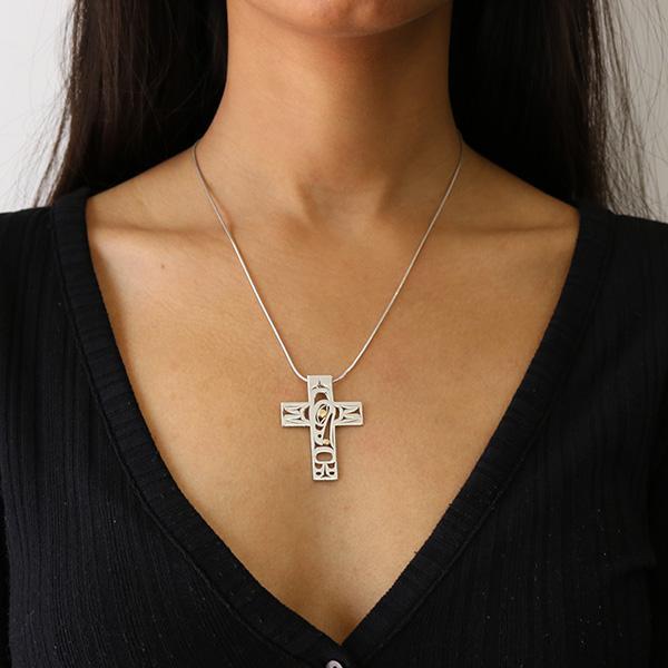 this gold and silver cross pendant is made using sterling silver and 18K gold. The pendant is shaped like a large cross and has cutout designs that depict the Raven.