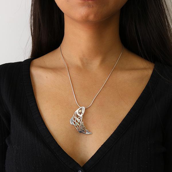 This sterling silver and 18K gold fish pendant is shaped like has cutouts in it that depict the Salmon.