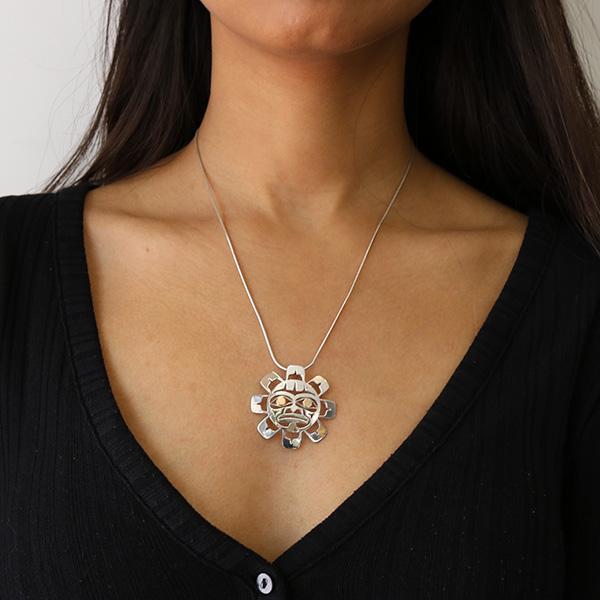 This Sun pendant is made from sterling silver and 18K gold. The pendant is shaped like and has cutouts that have been cast into it that depict the Sun. The eyes of the Sun are made from 14K gold.