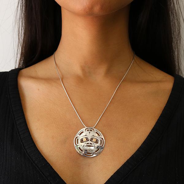 This cutout Moon pendant is made from sterling silver and 18K gold and has a circle shape. There are cutout designs made in the pendant that depict the Moon and the eyes of it are made from gold.