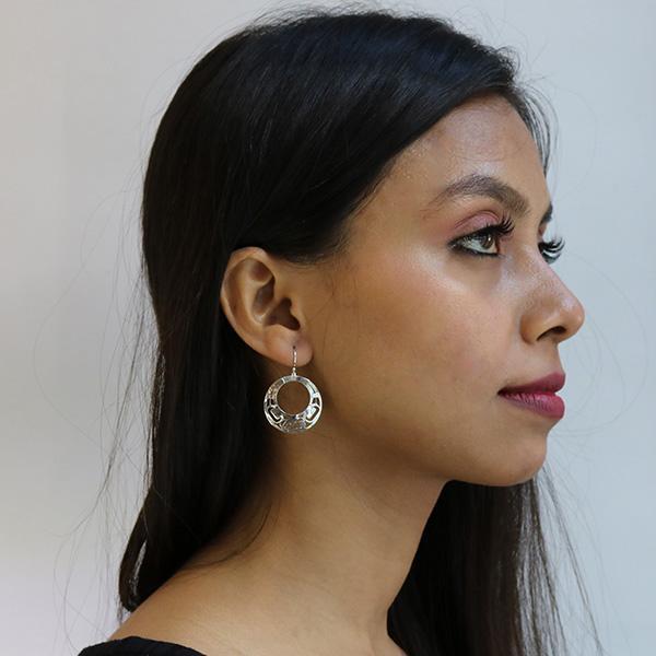 These cutout, circle dangle earrings are made from sterling silver and have circular hangs with a large, circle cutout. There are intricate cutout designs that depict the Raven on the surface of the hangs.