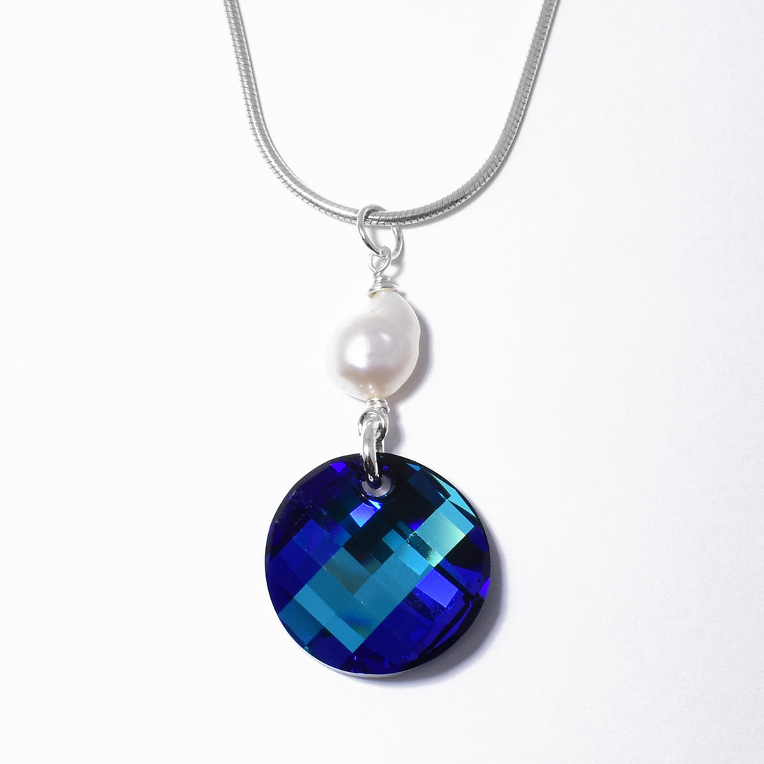 This Swarovski crystal pendant is made from sterling silver, freshwater baroque pearl and bermuda blue Swarovski crystal. The crystal has a large, circle shape and is dangling from a large, baroque pearl.