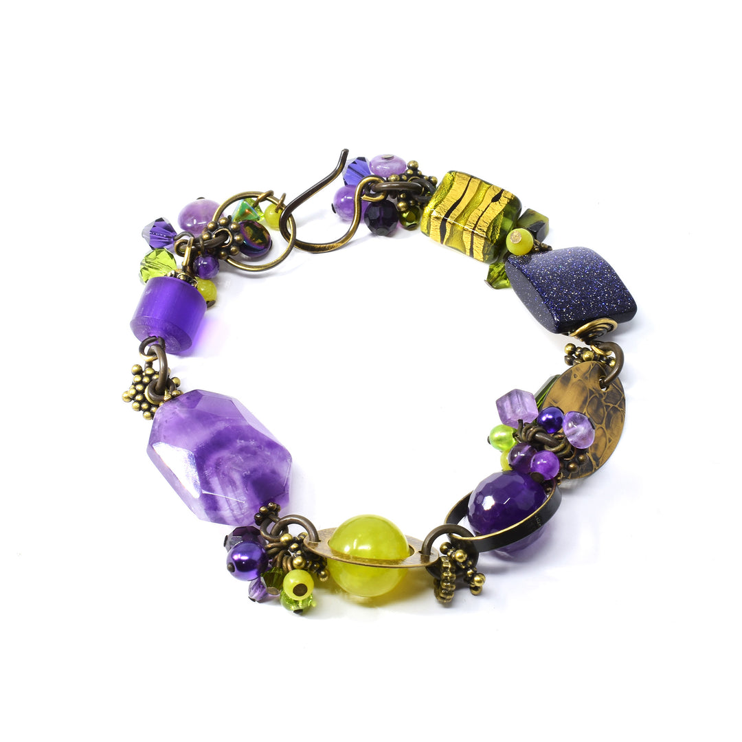 This unique beaded crystal bracelet is made from serpentine jade, Austrian crystal, freshwater pearls, yellow turquoise, purple goldstone, amethyst, peridot, glass, resins, and antique brass. There are beads and charms with different shapes, designs and materials that run along the entire piece.