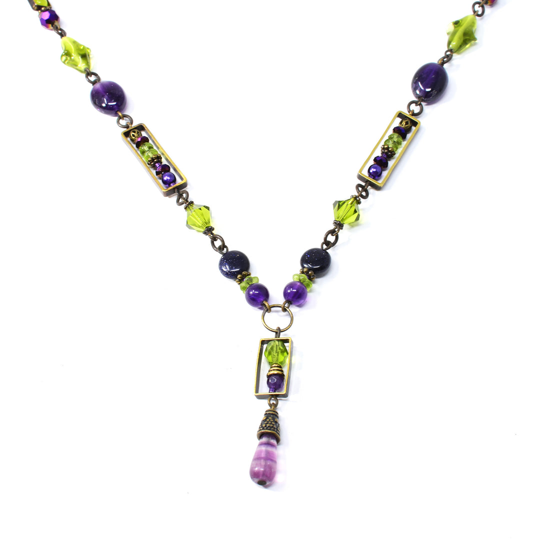 This beaded crystal necklace is made from serpentine jade, Austrian crystal, amethyst, peridot, fluorite, glass and antique brass. The beads have different shapes, designs and martials and wrap around the entire piece. There is a beaded lariat pendant with an unique amethyst bead at the bottom.