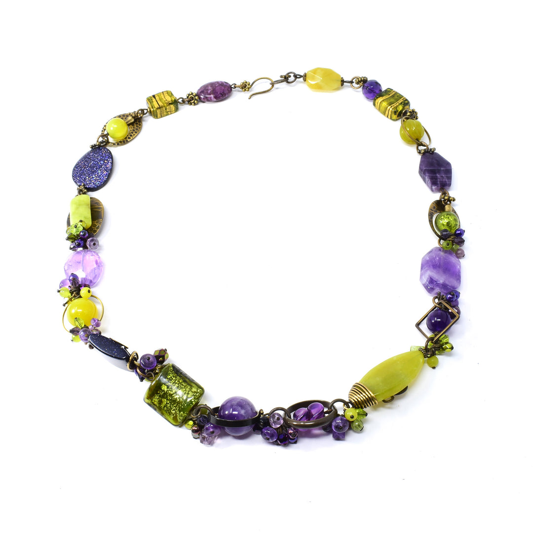 This beaded crystal necklace is made from serpentine jade, Austrian crystal, amethyst, peridot, fluorite, glass and antique brass. The beads have different shapes, designs and martials and wrap around the entire piece. 