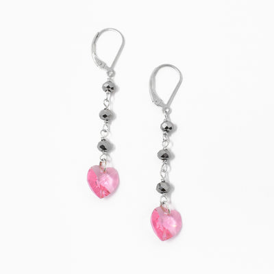 Pink Crystal Heart Dangle Earrings with Charcoal Roundels. At the end of each earring is a pink crystal in the shape of a heart. Above the heart is a chain with 3 charcoal roundels leading up to the hook of the earring.