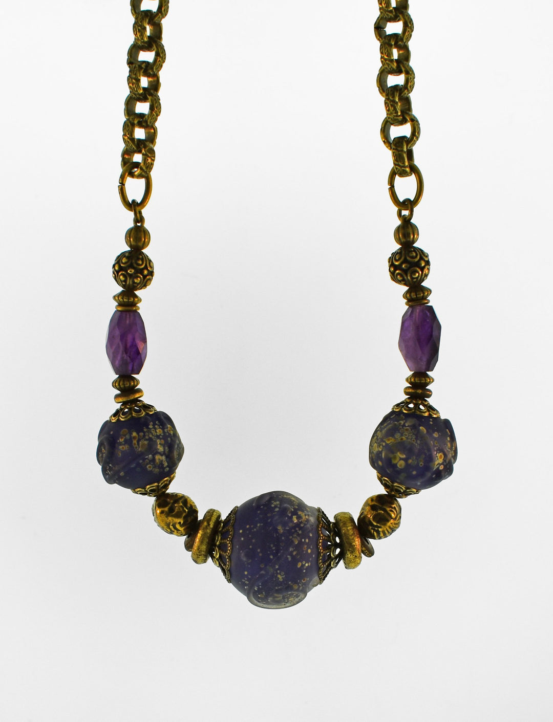 This beaded brass chain necklace is made from hand worked brass, lampworked brass and amethyst gemstones. There are three large purple and gold, glass beads with two amethyst beads and a chunky brass chain.