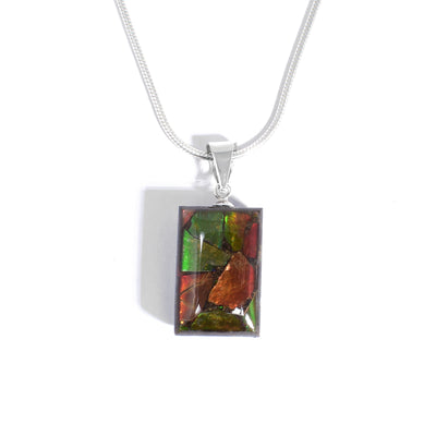 Pendant by Aryn Bowers. He has encased flakes of ammolite in resin to create it. Double-sided, each side has a unique display of ammolite. Sterling silver bail. Pendant measures 1" x 0.44" including bail.