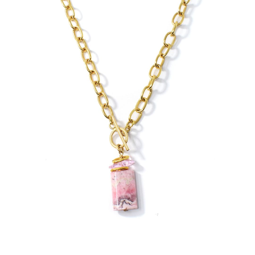 This crystal necklace with pendant is made rom 14K gold fill, pink Swarovski crystal and a large rhodonite gem. The pendant is wide, rectangular and made from rhodonite with swirling pink, designs on it. The chain is chunky and has circle shaped, gold links; there is pink cristal above the gemstone pendant.