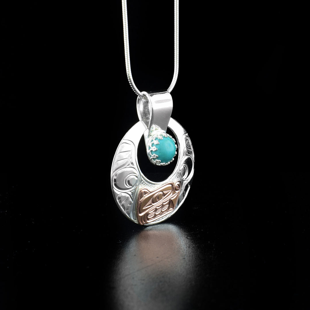 Round cut out bear pendant hand-carved by Coast Salish and Cree artist Richard Lang. The head of the bear is done in 14K rose gold and the rest of the piece is made of sterling silver. Richard has set turquoise at the bottom of the bail. Pendant measures 1.4" x 1.2" including bail. Chain not included.