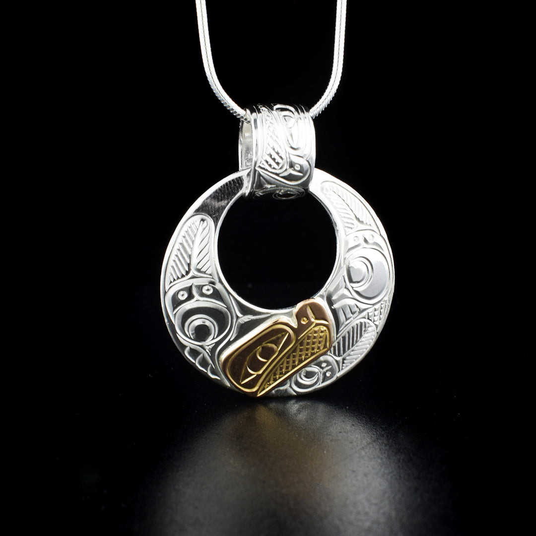 Round cut-out eagle pendant hand-carved by Coast Salish and Cree artist Richard Lang. Made of 14K gold and sterling silver. Pendant measures 1.38" x 1.25" including bail. Chain not included.