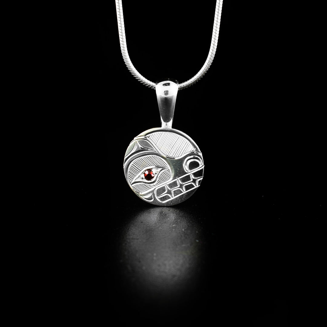 Round Silver Bear Pendant with Garnet hand-carved by Haisla artist Hollie Bartlett. She used sterling silver to create this piece and set a garnet in the eye of the bear. Pendant measures 1" x 0.60" including bail. Chain not included.