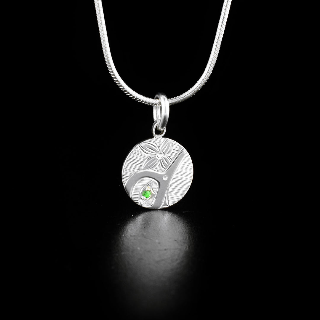 Round Silver Tsavorite Hummingbird Pendant hand-carved by Haisla artist Hollie Bartlett. She used sterling silver to create this piece and set a tsavorite in the hummingbird's eye. Pendant measures 0.70" x 0.50" including bail. Chain not included.