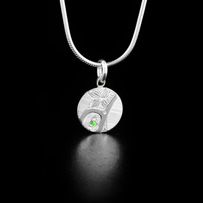 Round Silver Tsavorite Hummingbird Pendant hand-carved by Haisla artist Hollie Bartlett. She used sterling silver to create this piece and set a tsavorite in the hummingbird's eye. Pendant measures 0.70" x 0.50" including bail. Chain not included.
