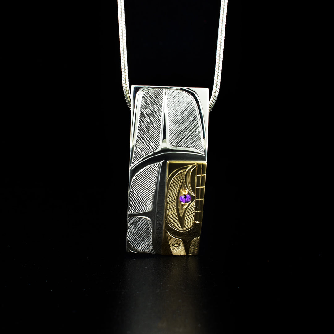 Unique rectangular orca pendant hand-carved by Haisla artist Hollie Bartlett. She used sterling silver and 14K gold to create this piece and set an amethyst in the orca's eye. Pendant measures 1.63" x 0.56". Hidden bail on back. Chain not included.