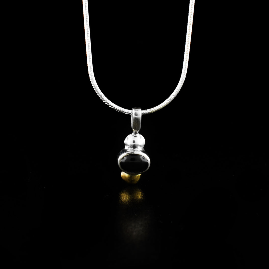 This black onyx pendant is made from sterling silver, 14K gold and a black onyx gemstone. The gem is oval shpaed and set in silver; there is a smaller gold oval below the gem.