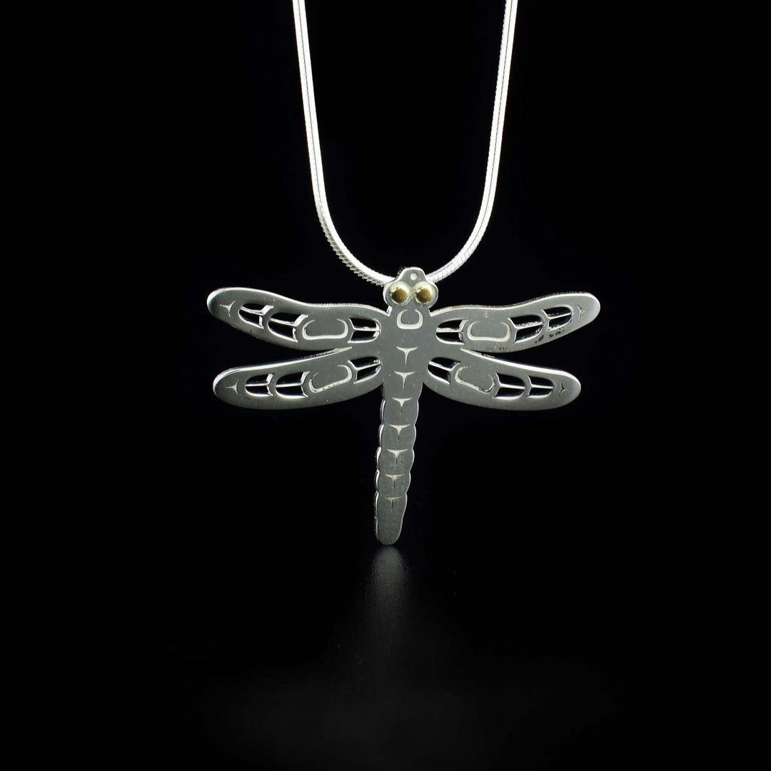 This Dragonfly pendant is made from sterling silver and 18K gold. The piece is shaped liek and has carving and cutout designs on it depicting the Dragonfly. They eyes of the legend are made from 18K gold.
