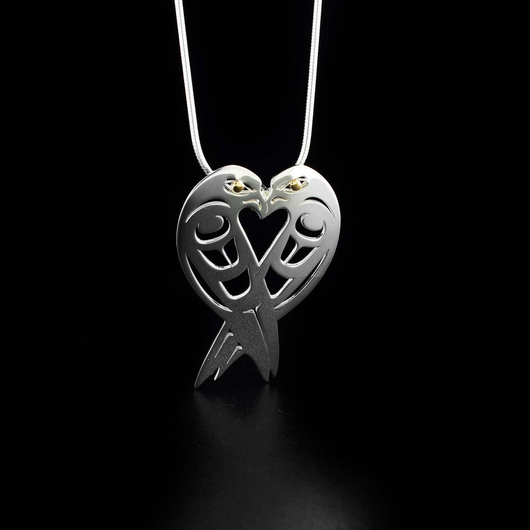 This unique heart pendant has two lovebirds facing towards each other, connecting to make a heart shape. Both lovebirds have a 18k gold accent in their eyes and intricate designs cut out along their bodies to represent their feathers.