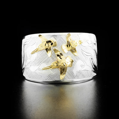 Hummingbird and calla lily bracelet hand-carved by Tlingit artist Fred Myra and contemporary Canadian artist Arlene Howk. 14K gold hummingbirds carved by Fred and sterling silver bracelet carved by Arlene. Bracelet is 6.75" long with 0.75" gap and is 1.50" wide. Ends are tapered.