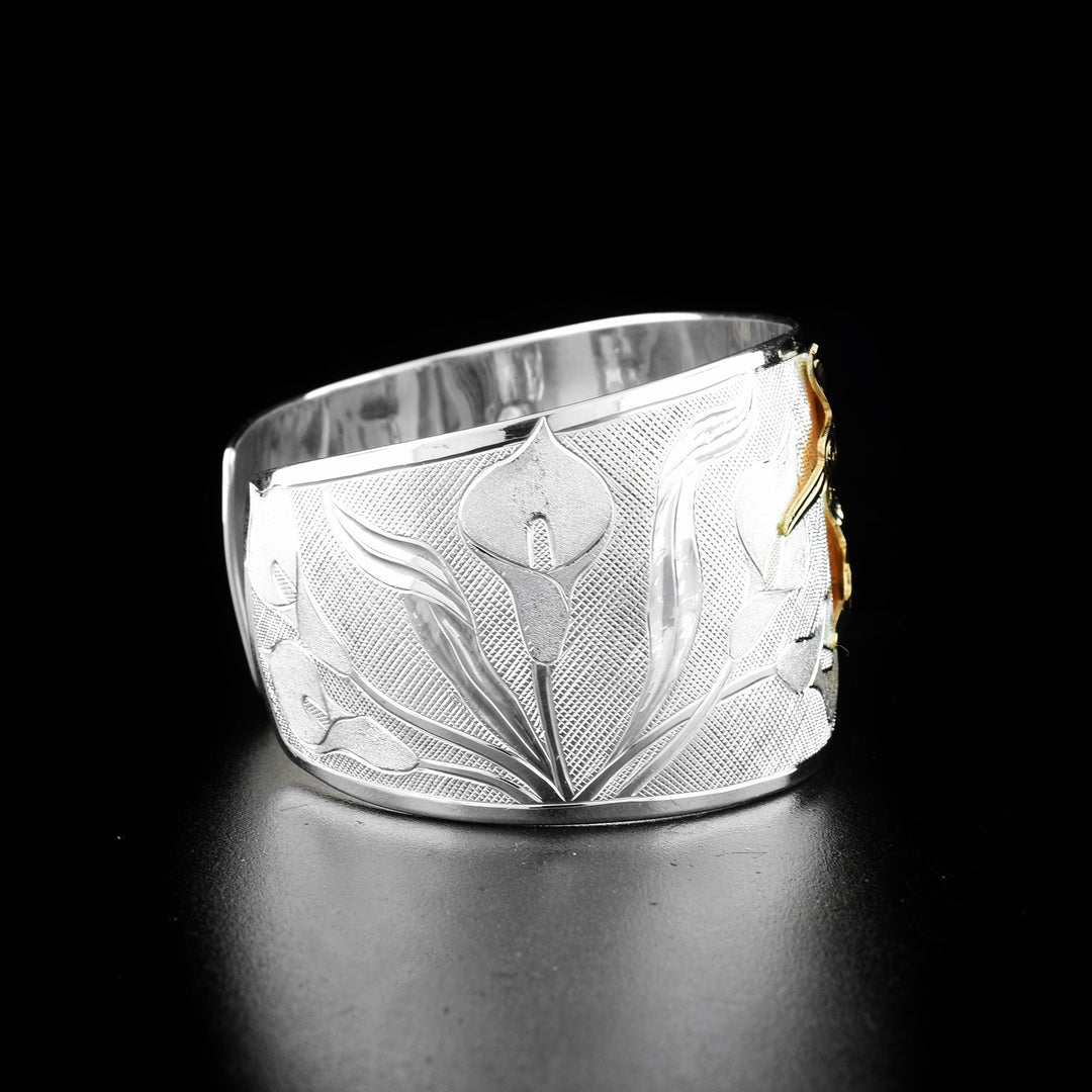 Hummingbird and calla lily bracelet hand-carved by Tlingit artist Fred Myra and contemporary Canadian artist Arlene Howk. 14K gold hummingbirds carved by Fred and sterling silver bracelet carved by Arlene. Bracelet is 6.75" long with 0.75" gap and is 1.50" wide. Ends are tapered.