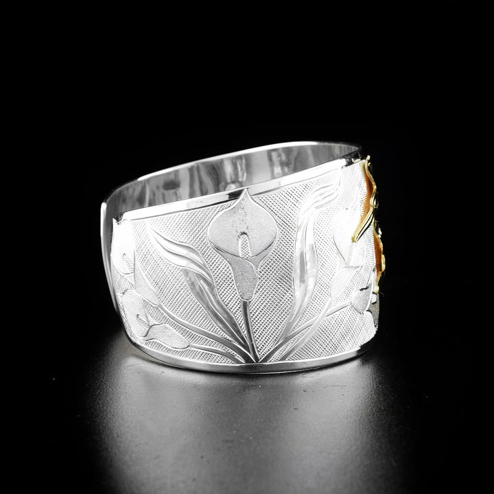 Hummingbird and calla lily bracelet hand-carved by Tlingit artist Fred Myra and contemporary Canadian artist Arlene Howk. 14K gold hummingbirds carved by Fred and sterling silver bracelet carved by Arlene. Bracelet is 6.75" long with 0.75" gap and is 1.50" wide. Ends are tapered.