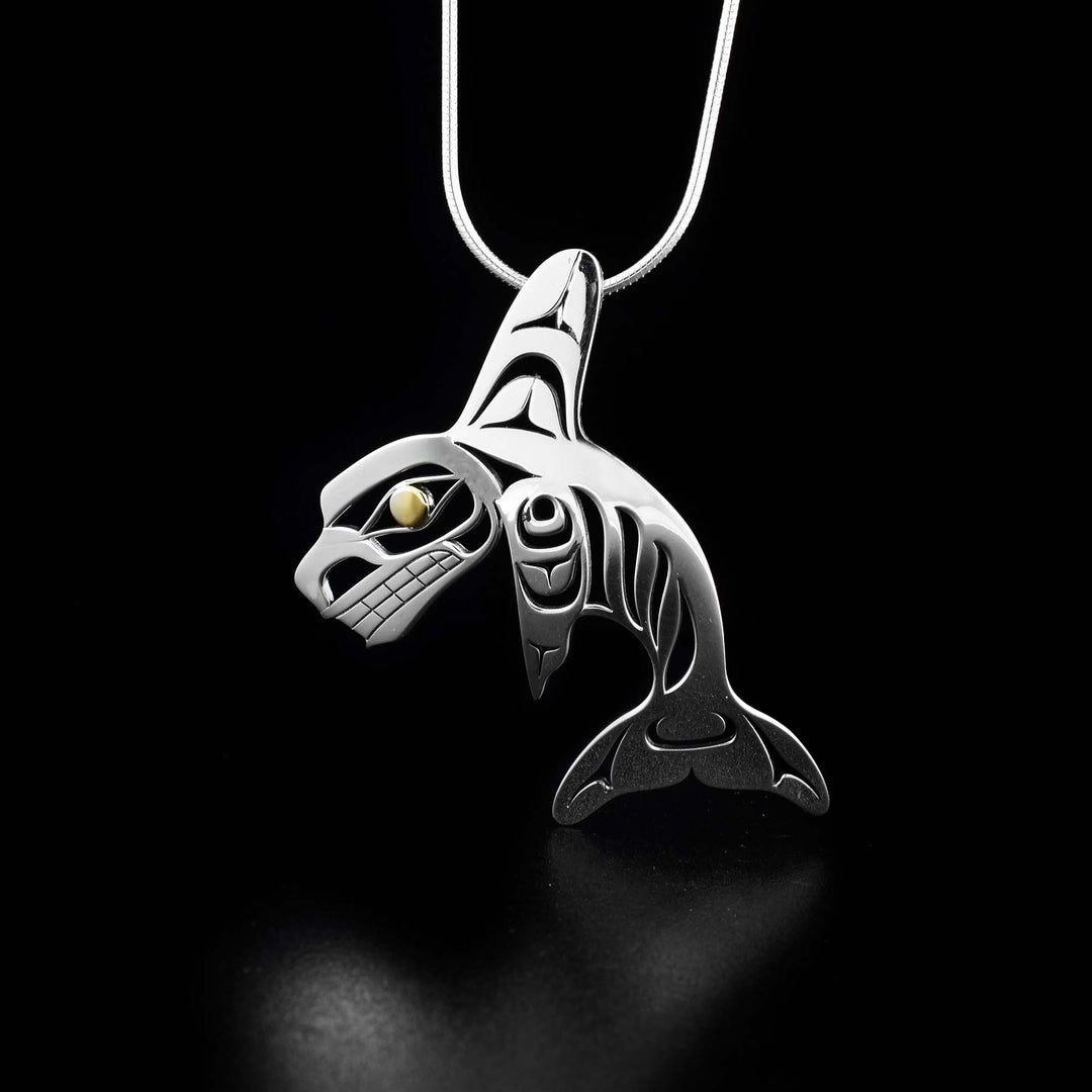 This Orca pendant is made from sterling silver and 18K gold. The pendant is shaped like and has cutout designs that depict the Orca. The eye of the Orca is made from 18K gold.