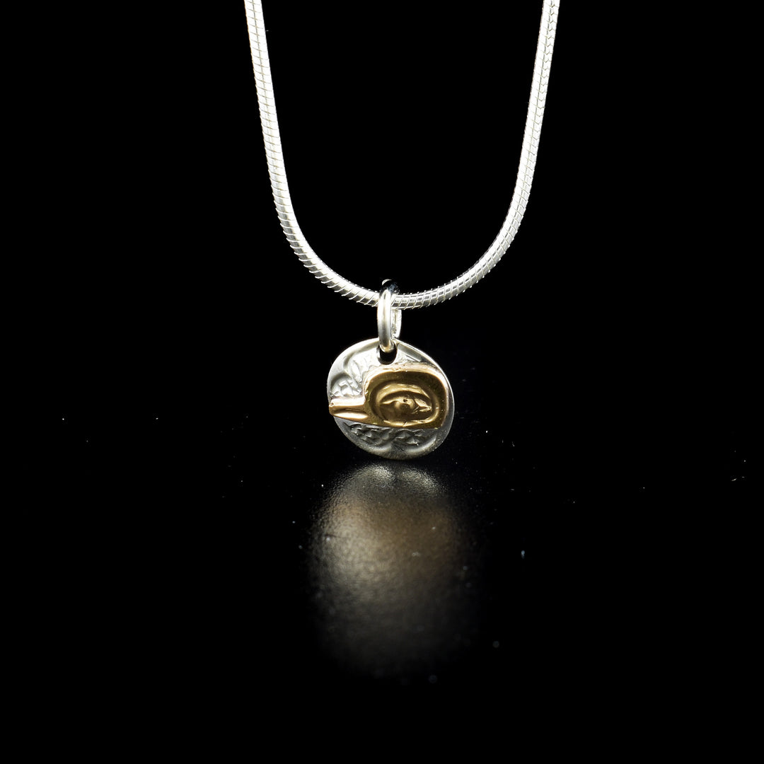 Small round hummingbird charm hand-carved by Kwakwaka'wakw artist Carrie Matilpi. Made of 14K gold and sterling silver. Charm measures 0.50" x 0.40" including bail. Chain not included.