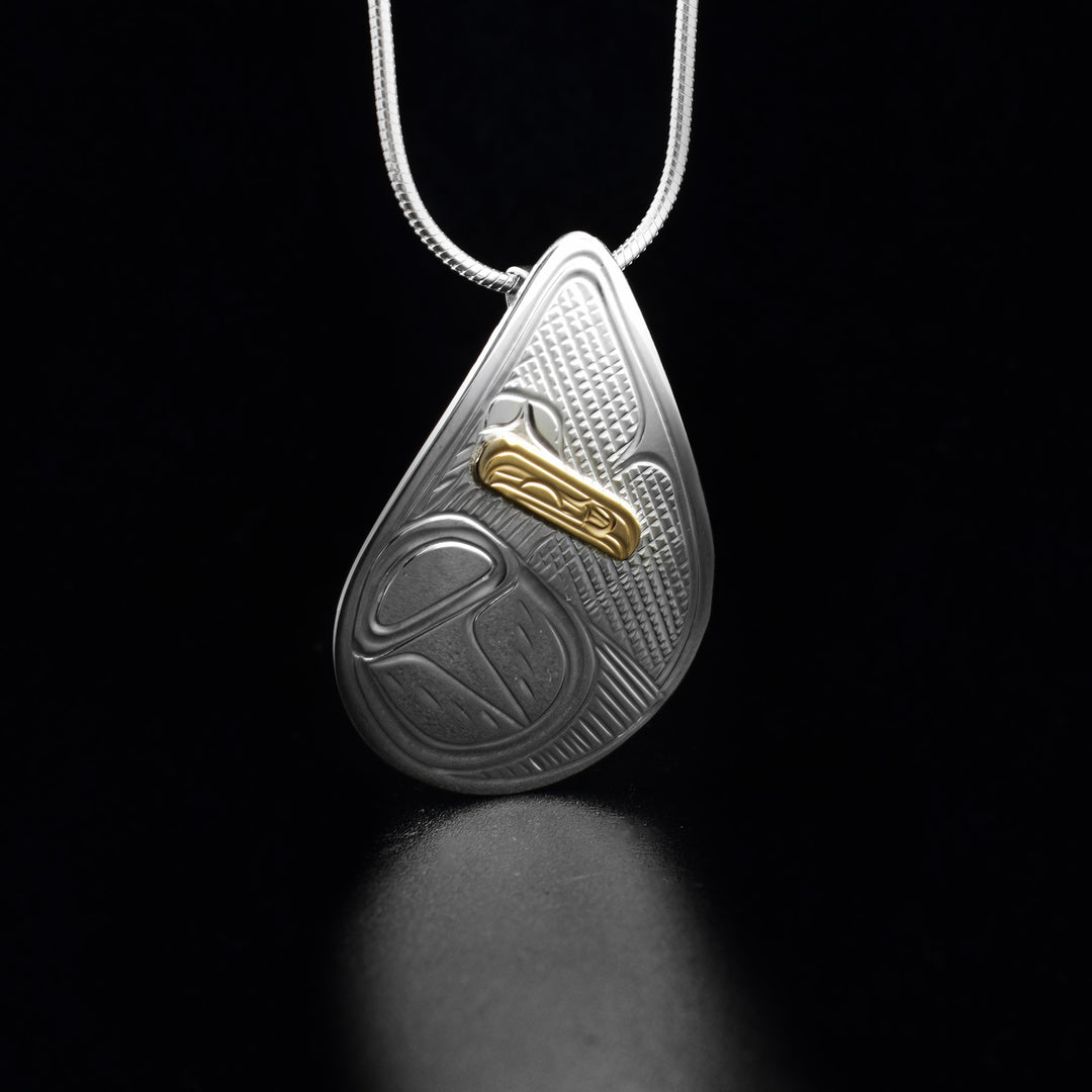 This Raven pendant is made form sterling silver, 14K gold and has a teardrop shape. There are carvings on the surface of the pendant depicting the Raven and the head of the legend is made from gold.