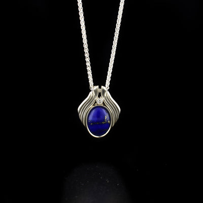 Silver Lapis Lazuli Pendant with Canadian Diamond handcrafted by artist Dennis Kangasniemi. He has set lapis lazuli in sterling silver. Above the lapis lazuli is a Canadian diamond in a sterling silver bezel setting. Pendant measures 0.75" x 0.63". Chain not included.