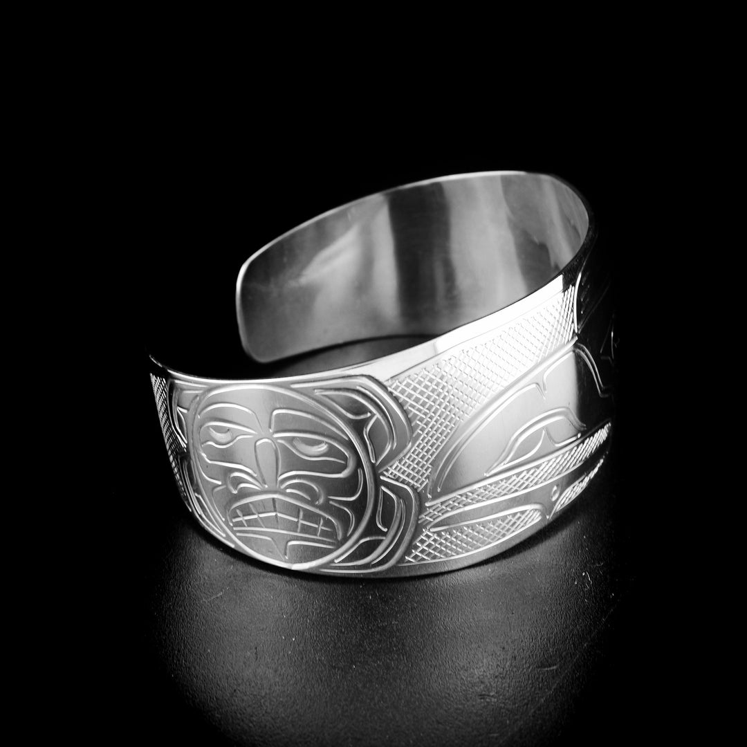 Tapered raven and sun bracelet hand-carved by Kwakwaka'wakw artist John Lancaster. Made of sterling silver. Bracelet is 6.15" long with 0.80" gap and has width of 1". Tapered ends.