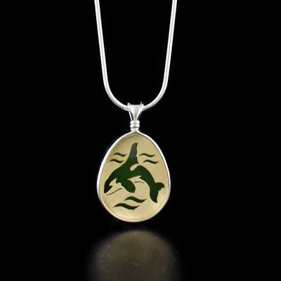 Unique Small BC Jade Bull Orca Pendant handcrafted by artist Dennis Kangasniemi. He engraves his original designs on 14K yellow gold panels. The panels are then soldered in heavy sterling silver pendant settings and finished with a backdrop of A+ grade BC jade. The artist achieves his BC wildlife jewellery by precise hand-cutting. Pendant measures 1.25" x 0.75" including hook. Chain not included.