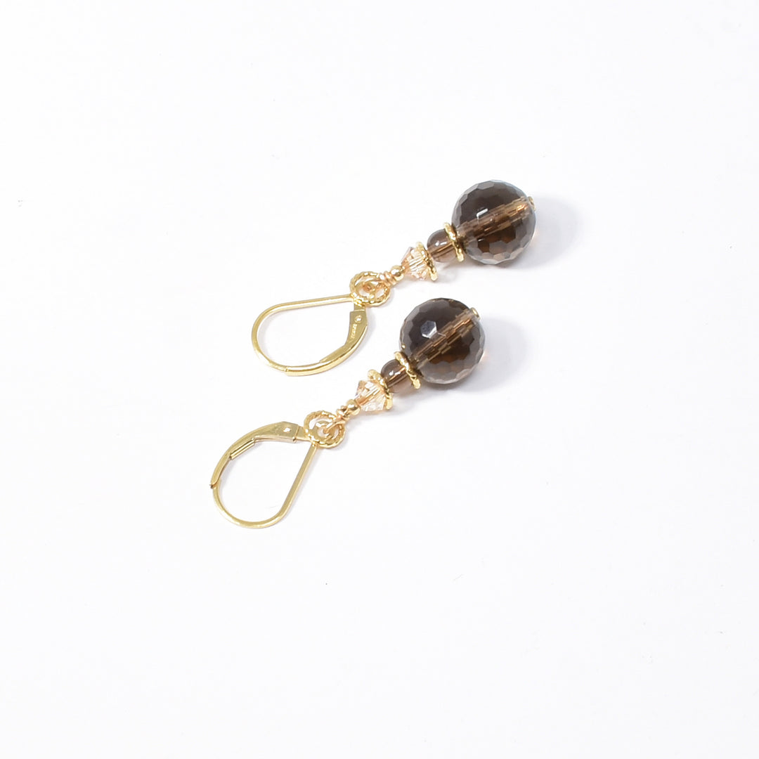 Stunning Smoky Quartz and Swarovski crystal drop earrings handcrafted by artist Karley Smith. Earrings made of gold-plated wire and adornments, smoky quartz and Swarovski crystals in Golden Shadow. Ear hooks are gold-filled. Each earring measures 1.50" x 0.40" including hook.