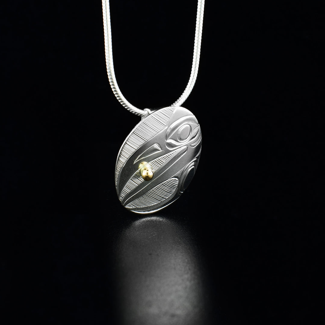 Sterling silver and 14K gold oval raven pendant hand-carved by Haisla artist Hollie Bartlett. Pendant measures 1" x 0.75". Hidden bail on back. Chain not included.