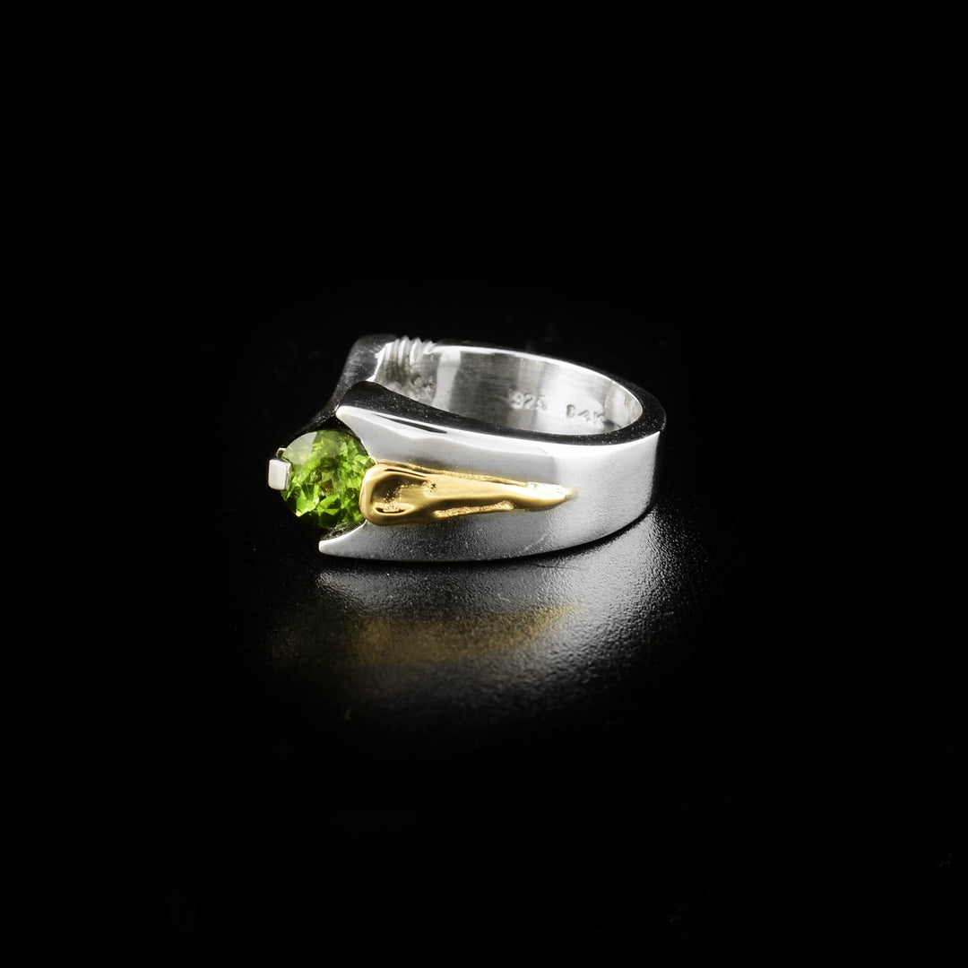 This unique peridot ring is made form sterling silver, 14K gold and peridot gemstones. The top section of the ring is a flat bar with a peridot gem embedded at the end of it. There is a decorative gold piece on the other side of the gem.