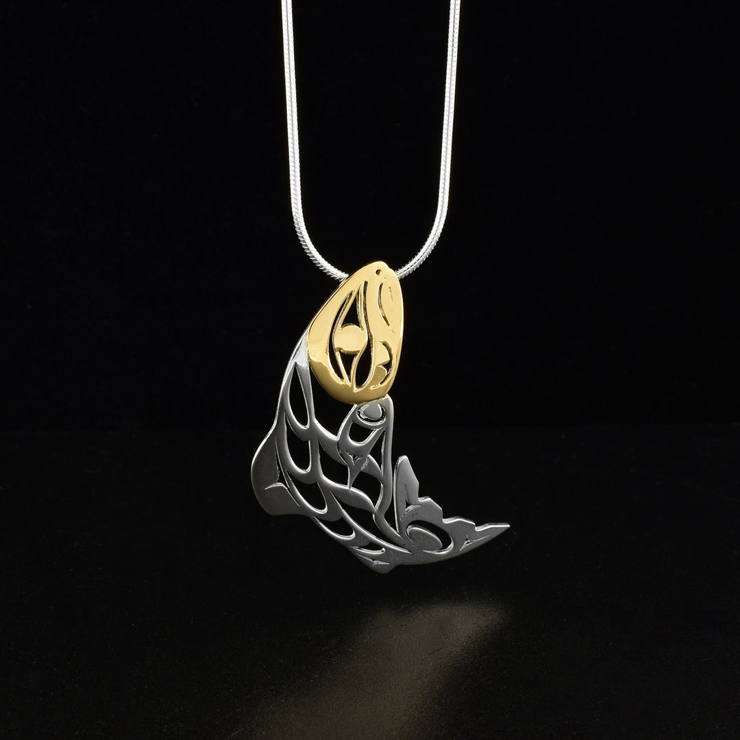 Pierced salmon pendant by Tahltan artist Grant Pauls. He has used 18K gold for the face of the salmon and sterling silver for the rest of the piece. Pendant measures 1.75" x 0.69". Hidden bail on back. Chain not included.