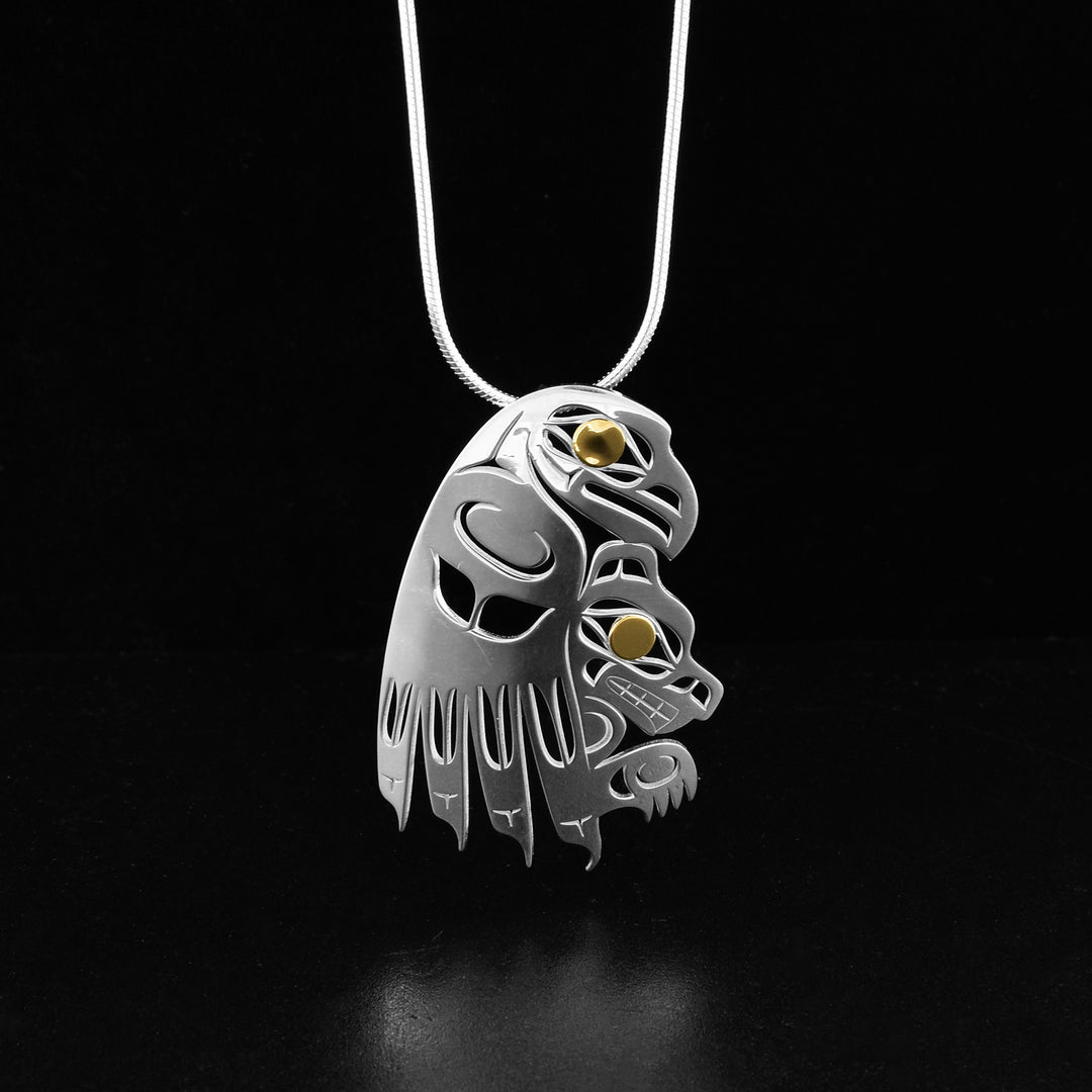 Eagle and Wolf pendant by Tahltan artist Grant Pauls. He has used sterling silver to create this piece and accented the eye of the wolf and the eye of the eagle with 18K gold. Pendant measures 1.75" x 1.13". Hidden bail on back. Chain not included.