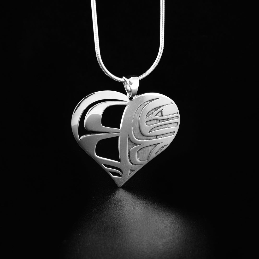  Orca sterling silver heart pendant necklace  by Grant Pauls. The pendant is in the shape of a heart. The artist has cut out the left side of the pendant into intricate designs. The right side of the pendant has been laser cut into the profile of an orca's head facing towards the right. 