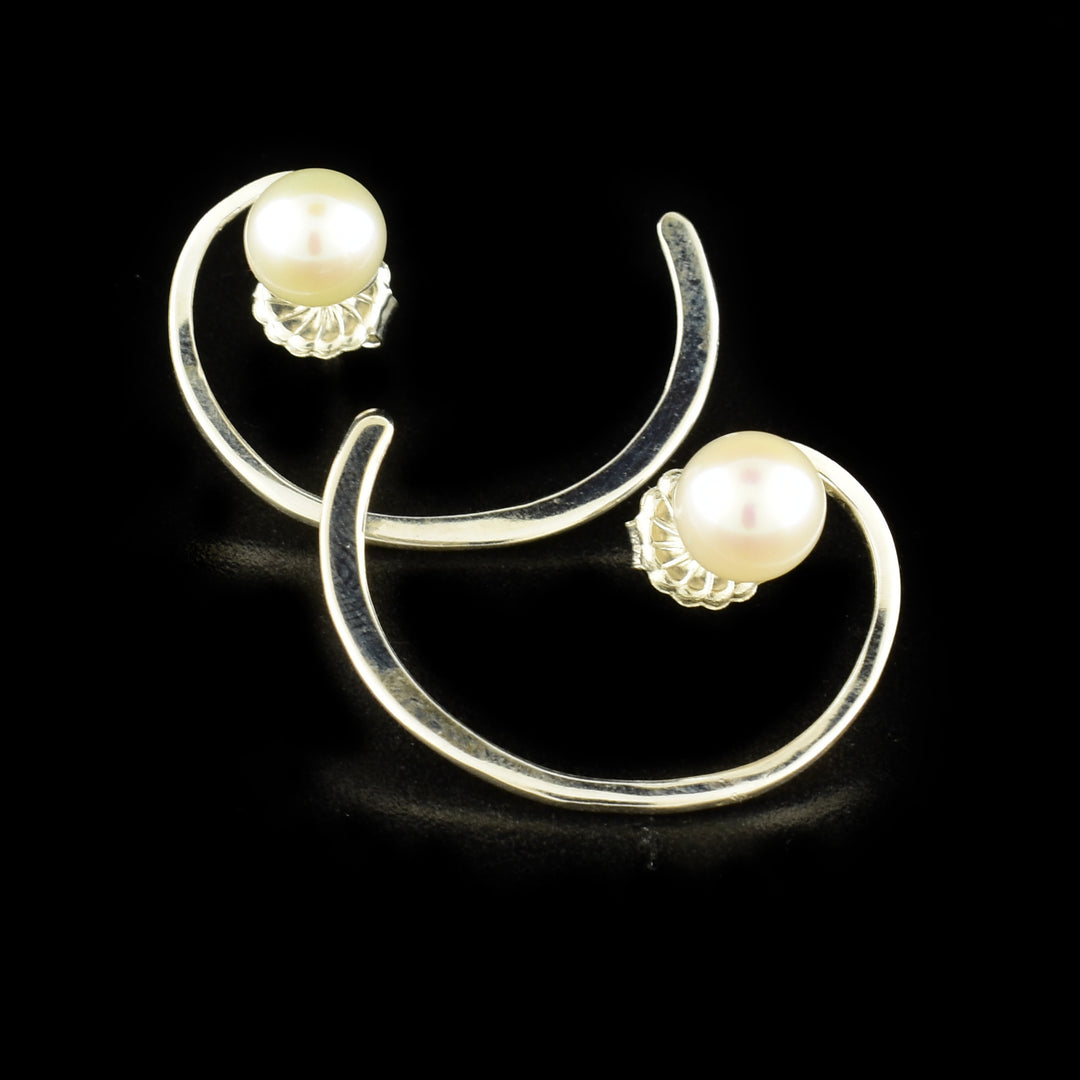 These elegant pearl hoop earrings are made from sterling silver and freshwater pearls. The pearls are placed at the top of the studs and the silver hoops have a swirly design that leaves a gap in the back of the piece.
