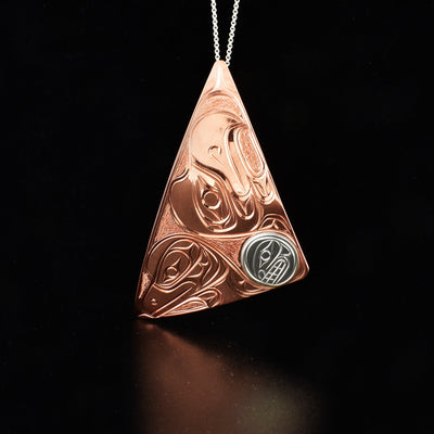 Copper Eagle, Moon, and Raven Triangle Pendant by Paddy Seaweed. The design depicts the profile of an eagle's head facing upward, the profile of a raven's head facing downward, and a the profile of a moon's face facing towards the raven. The moon is made out of sterling silver while the rest is made out of copper.