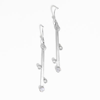Flat strips of silver with silver bobbles on sides hang from hooks. At end of each strip there is a cubic zirconia set in the metal. Each earring hangs 1.88” long including hook.