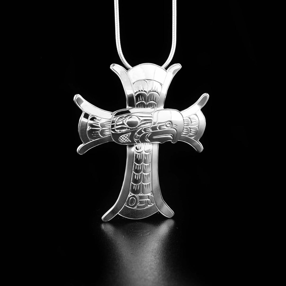 This sterling silver cross pendant is wide and the ends of it flare out and have designs on the ends. There are carvings on the surface depicting the Eagle with its face in the center and feather/design around the rest.